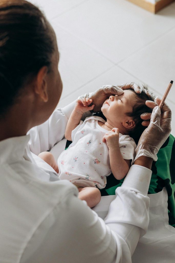 A healthcare professional gently examines a newborn baby indoors.